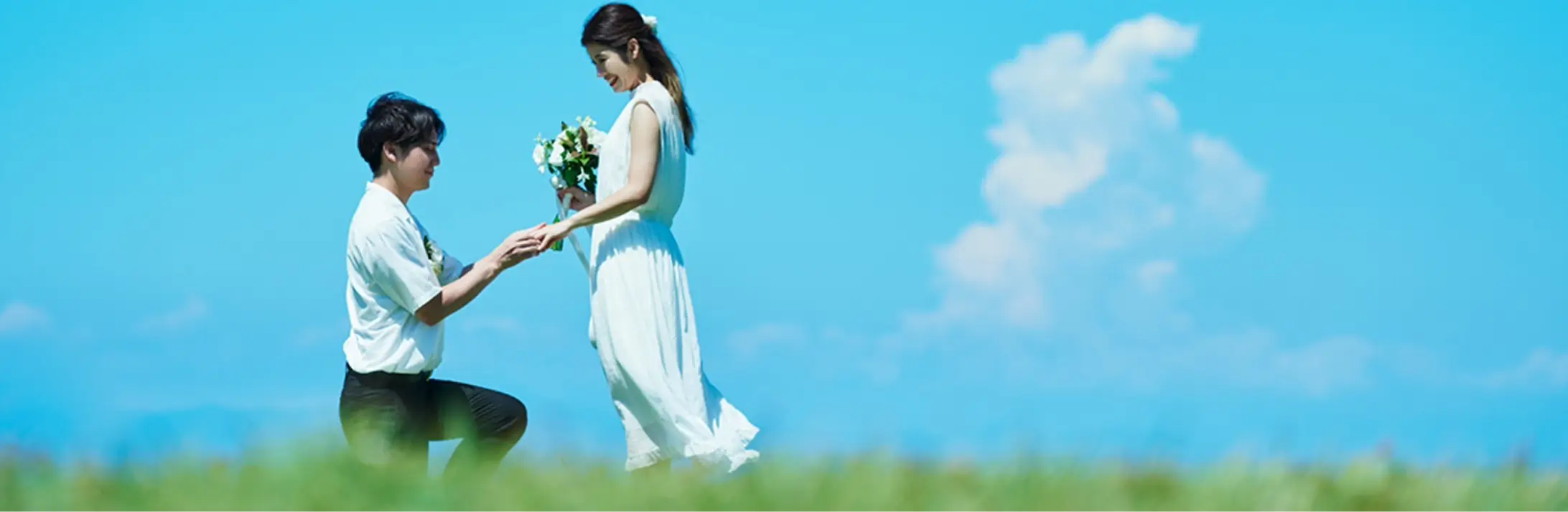 青空の下で花嫁が花婿に結婚指輪をはめてもらっている様子